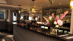 A bar area with a counter, bottles, glasses, and a decorative vase with flowers. - Riva Boutique Hotel & Restaurant (Helensburgh)
