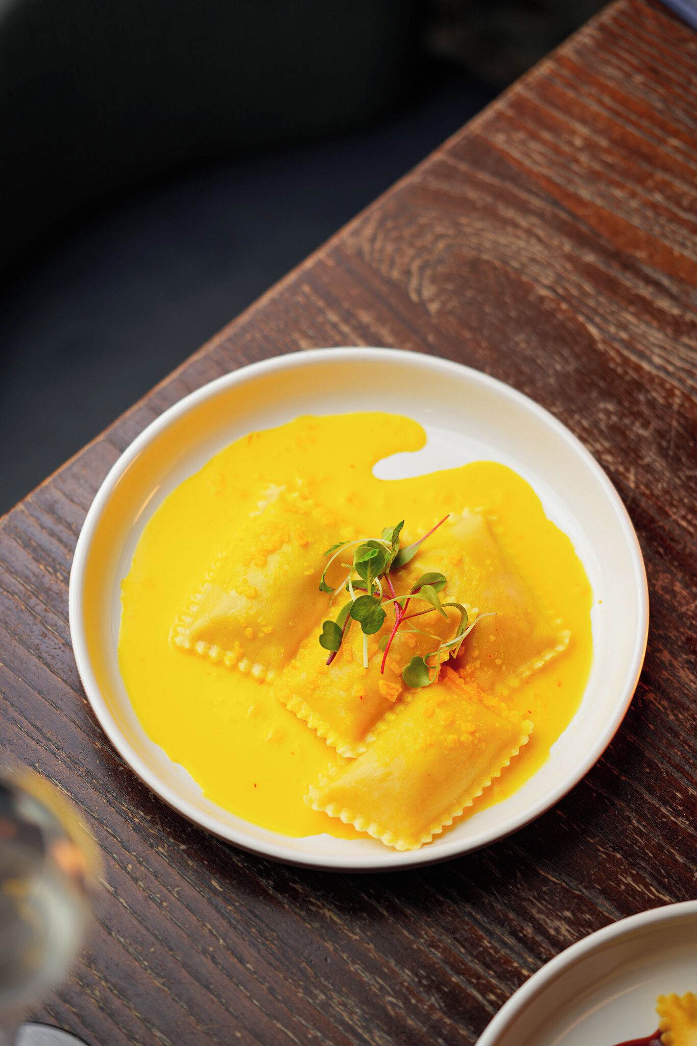 Plat de raviolis amb salsa groga i guarniments damunt d'un taulell de fusta.