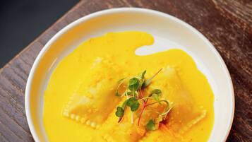 Prato de ravioli com molho amarelo e guarnições sobre uma mesa de madeira.