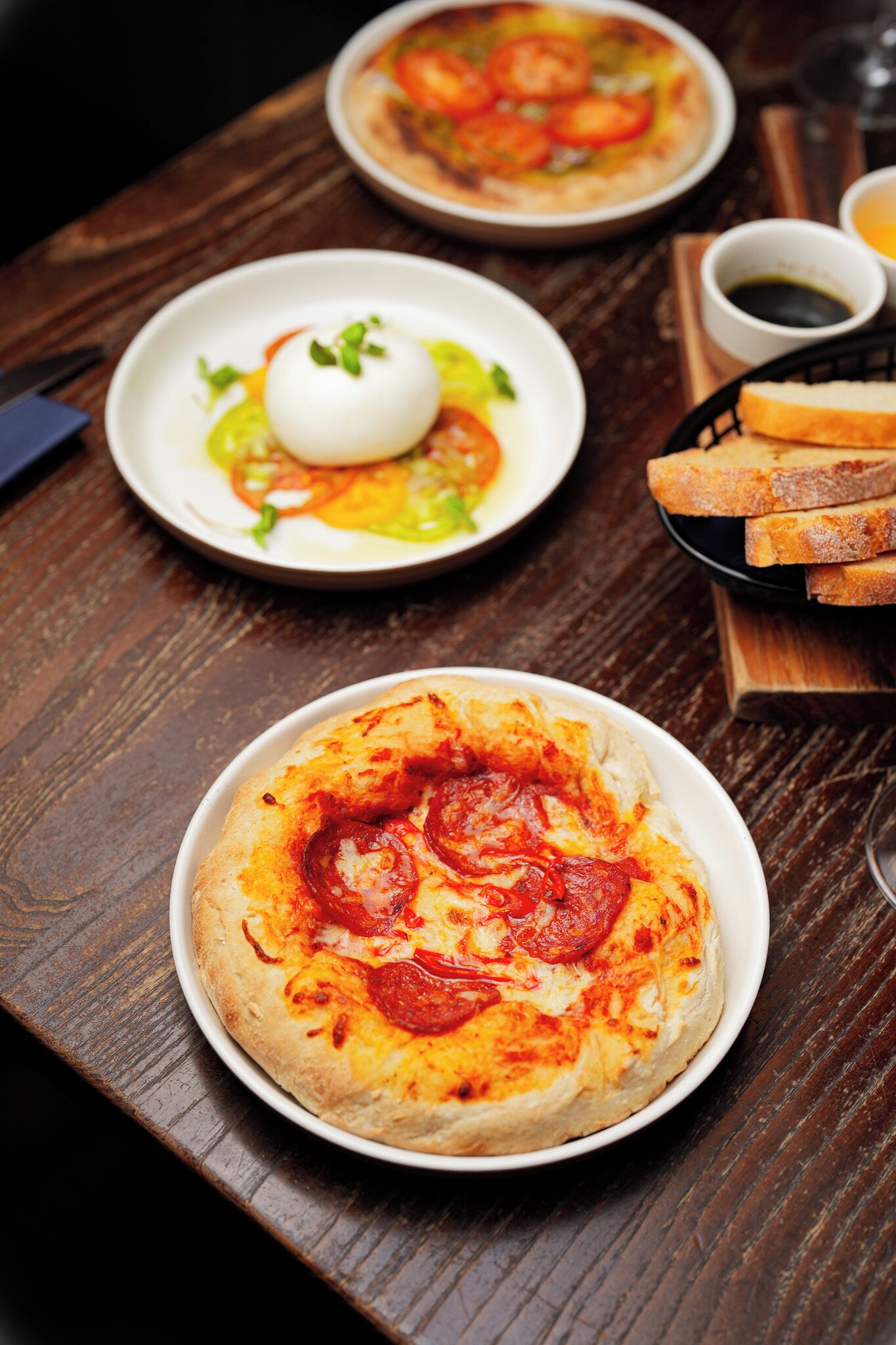 Uma mesa de madeira com dois pratos de comida, um com pizza e outro com ovo poché e vegetais.
