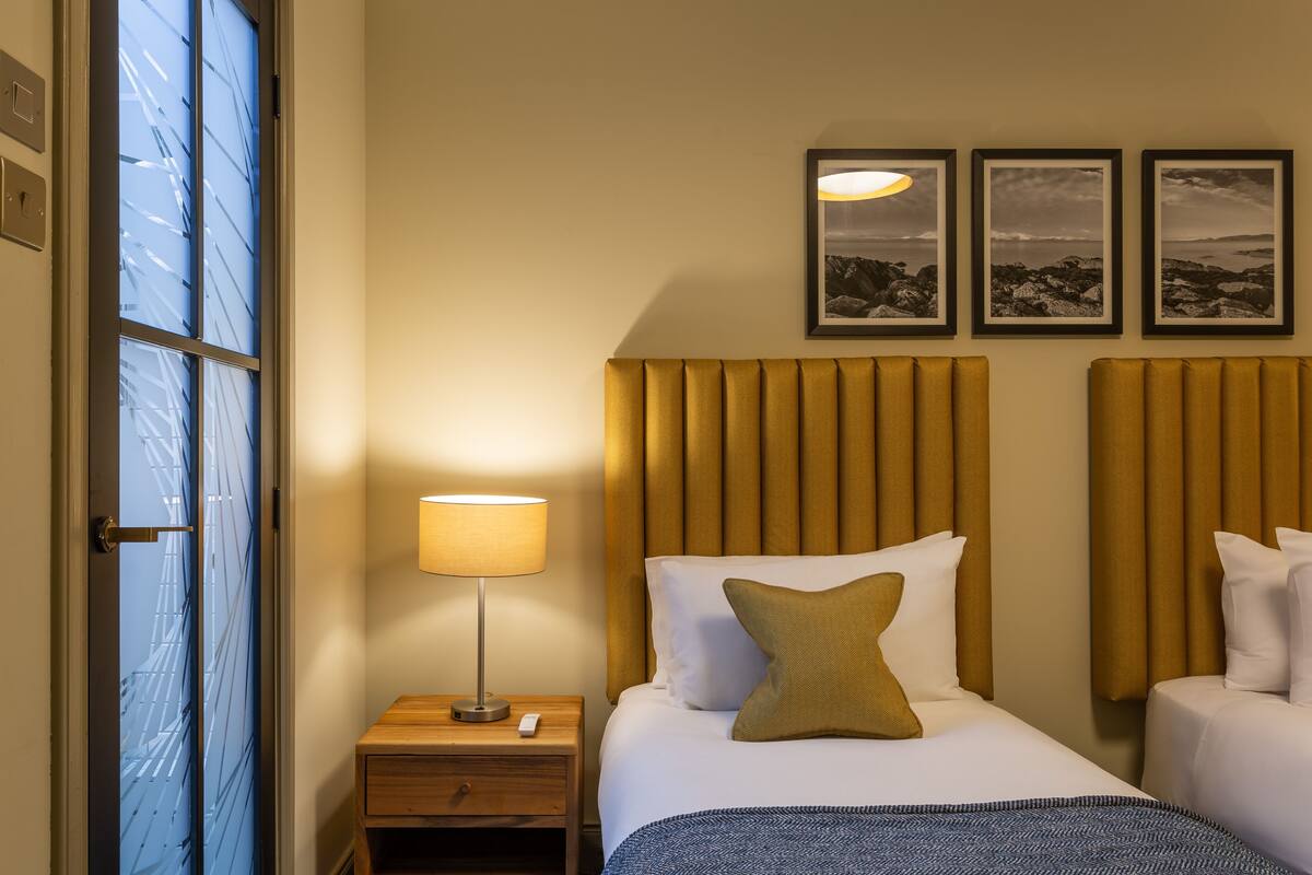 A hotel room with a bed, bedside table, lamp, and two framed pictures on the wall.