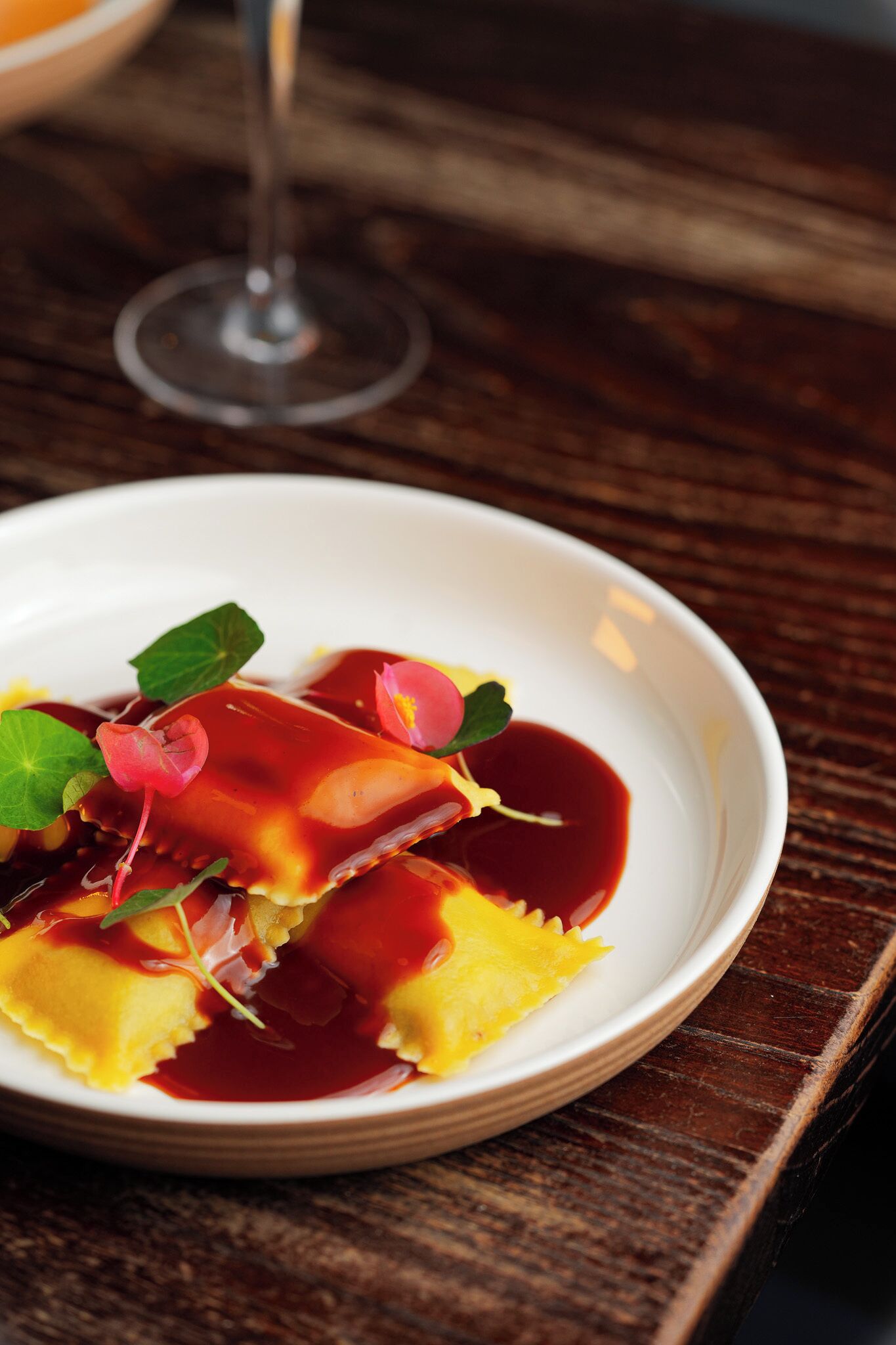 A white plate with ravioli and sauce on a wooden table.