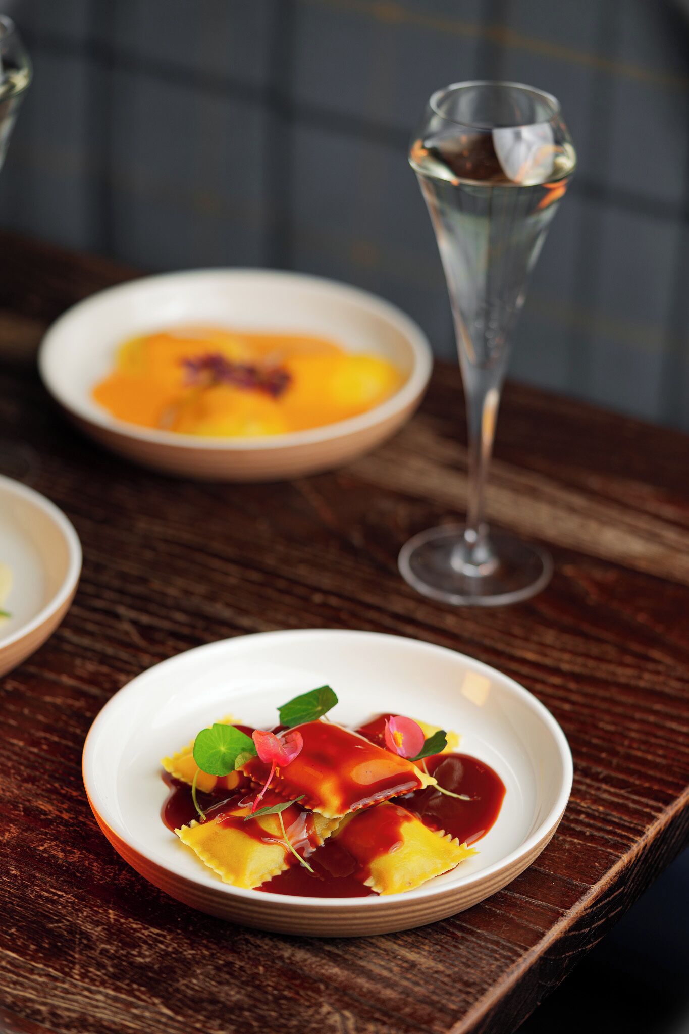 A dining table with a plate of ravioli and a glass of wine.