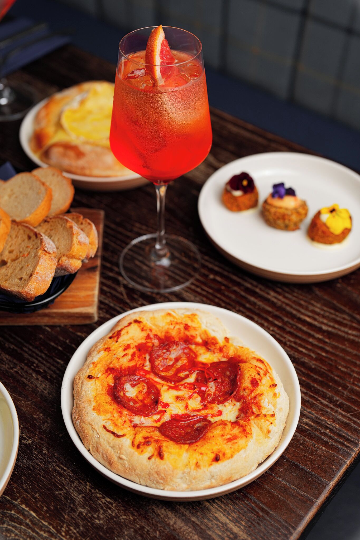 A table with a pizza, a glass of red drink, and some pastries.