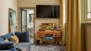 A hotel room with a sofa, a desk with a mirror, a flat-screen TV, and a window with curtains. - Riva Boutique Hotel & Restaurant (Helensburgh)