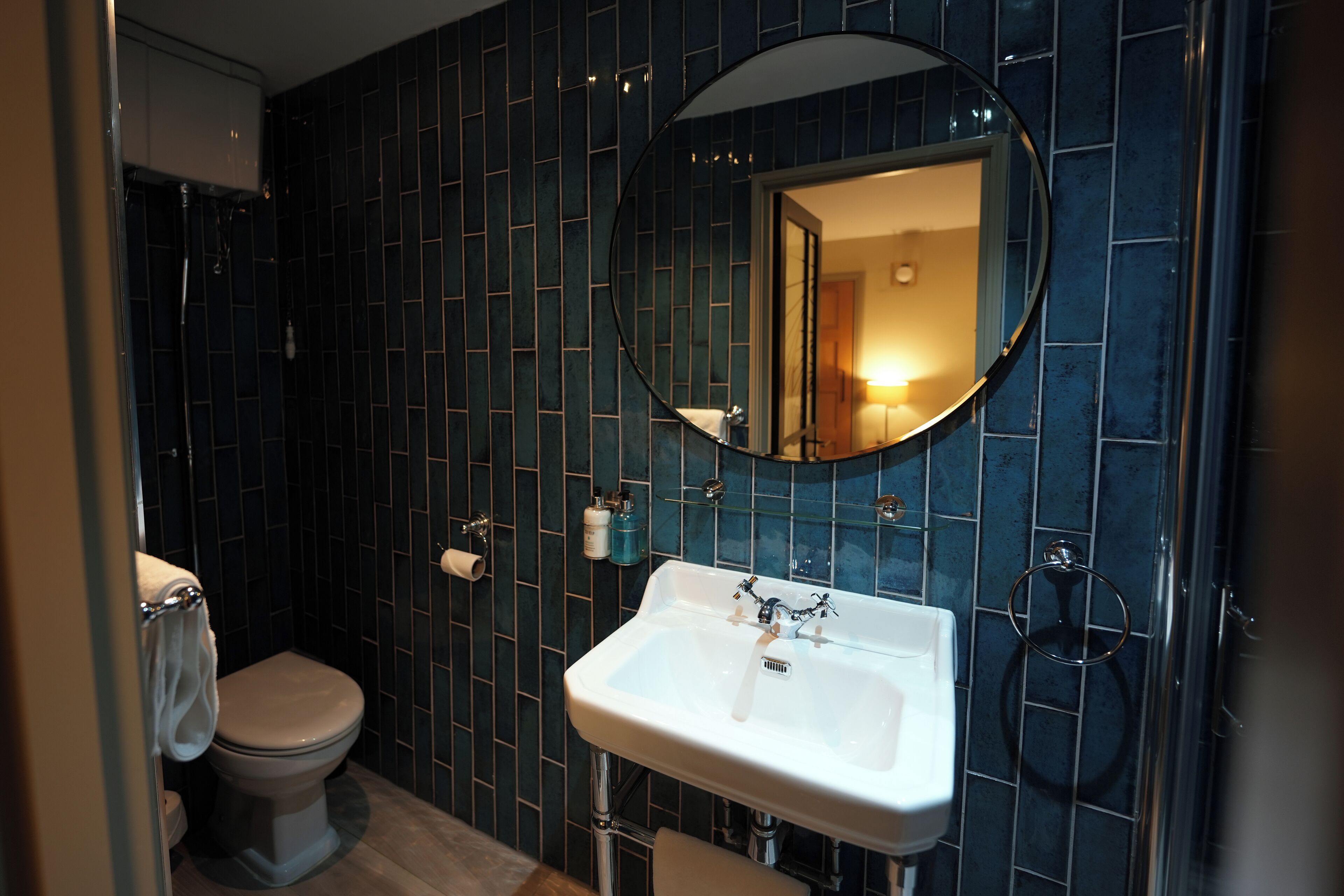 A bathroom with dark blue tiled walls, a white sink with a mirror above it, and a toilet.