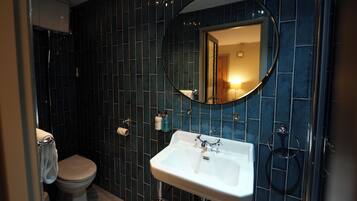 A bathroom with dark blue tiled walls, a white sink with a mirror above it, and a toilet.