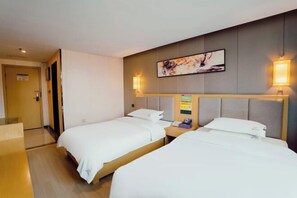 A hotel room with two beds, a bedside table with a phone, a wall-mounted artwork, and a door to the left.