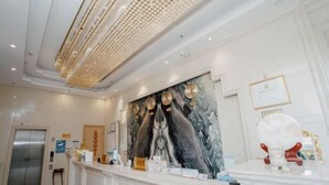 En hotellobby med en vägg av marmor, en receptionsdisk, ett inramat certifikat och en staty.