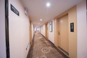 A hotel hallway with carpeted floors, doors on the right, and directional signs on the left. - Zheng'an Manfei Hotel (Guitar Culture Squaie Branch) (Zheng'an)