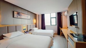 Ett hotellrum med två sängar, ett skrivbord, en tv och ett fönster med gardiner.