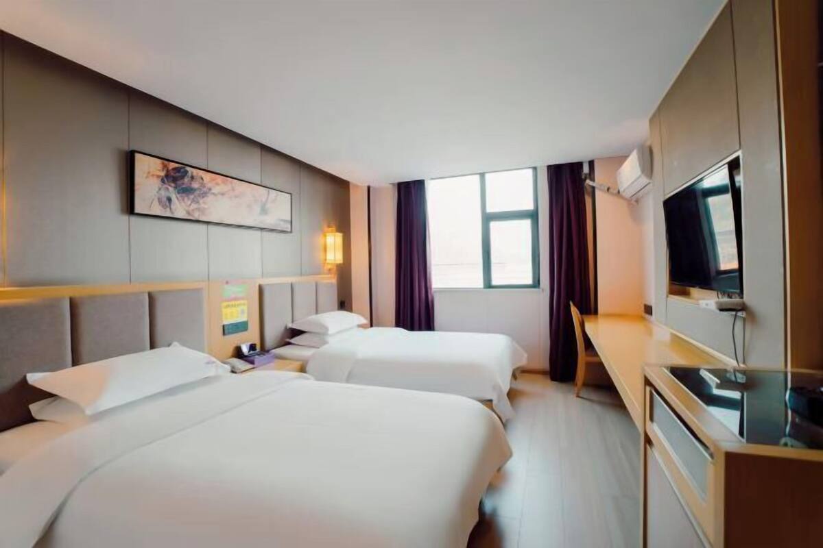 A hotel room with two beds, a desk, a TV, and a window with curtains.