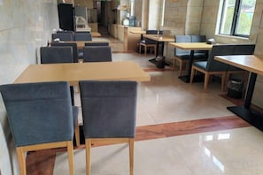 A dining area with tables and chairs, a kitchen in the background, and a window providing natural light. - Zheng'an Manfei Hotel (Guitar Culture Squaie Branch) (Zheng'an)