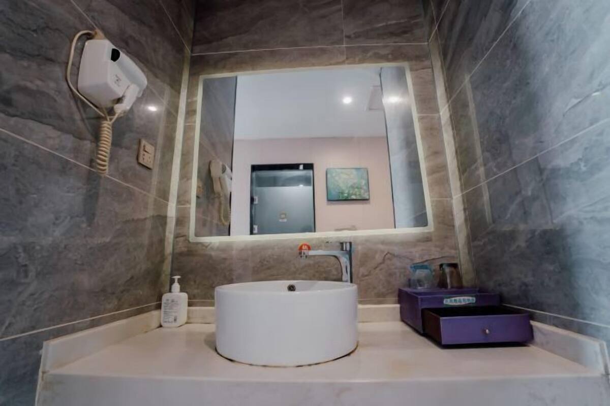 A modern bathroom with a white sink, a mirror, a hairdryer, and a purple storage box.
