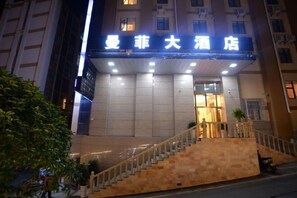 A hotel entrance with a sign in Chinese characters, a staircase, and a well-lit facade.