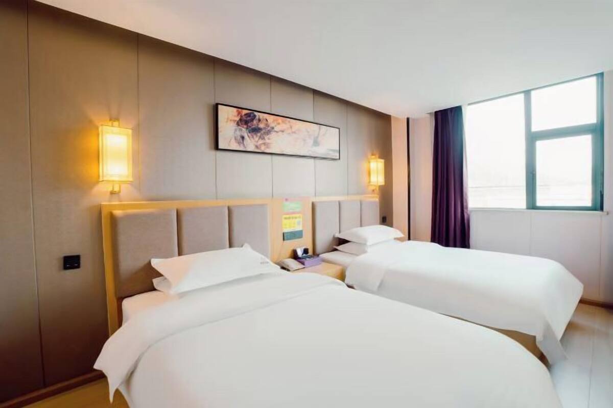 A hotel room with two beds, a headboard, wall-mounted artwork, and a window with curtains.