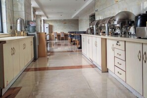 Uma cozinha ampla com bancada longa, vários eletrodomésticos e piso cerâmico.