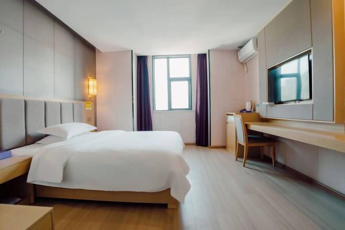 A hotel room with a bed, a desk, a chair, a TV, and a window.