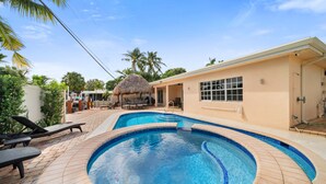 A swimming pool with lounge chairs, a thatched-roof structure, and a building with large windows. - Luxury Water Front, Heated Pool & Jacuzzi, 5br  (Pompano Beach)