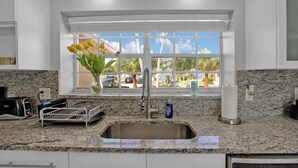 A kitchen with a granite countertop, stainless steel sink, and a window with a view of palm trees and parked cars. - Luxury Water Front, Heated Pool & Jacuzzi, 5br  (Pompano Beach)