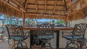 An outdoor bar area with a thatched roof, wooden beams, and metal chairs with striped cushions. - Luxury Water Front, Heated Pool & Jacuzzi, 5br  (Pompano Beach)