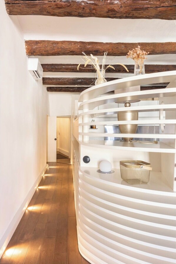 A modern kitchen with a curved white island, wooden beams on the ceiling, and a wooden floor.