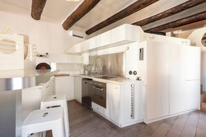 Une cuisine moderne avec des meubles blancs, des appareils en acier inoxydable et des poutres en bois apparentes.