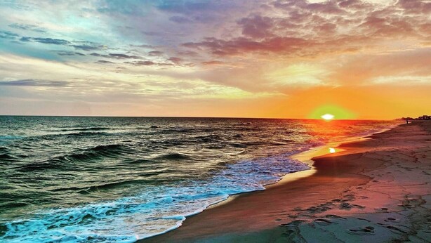 A beach with waves and a sunset.