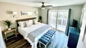 A bedroom with a bed, a ceiling fan, a TV, a balcony, and a potted plant.