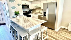A modern kitchen with a marble countertop, stainless steel appliances, and a white color scheme.