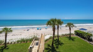 Vista de la playa con palmeras, un paseo marítimo de madera y sombrillas.