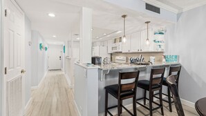 Una cocina moderna con armarios blancos, una isla de mármol y taburetes de bar.