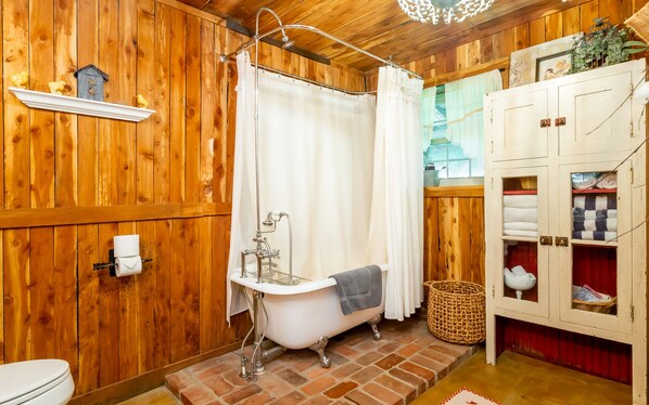 Un baño rústico de madera con una bañera tipo patas de león, cortina de ducha y un mueble de madera con estantes.