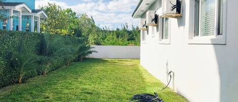 Ein gepflegter Rasen mit einem Gartenschlauch, ein weißes Gebäude mit Fenstern und ein blaues Gebäude im Hintergrund.