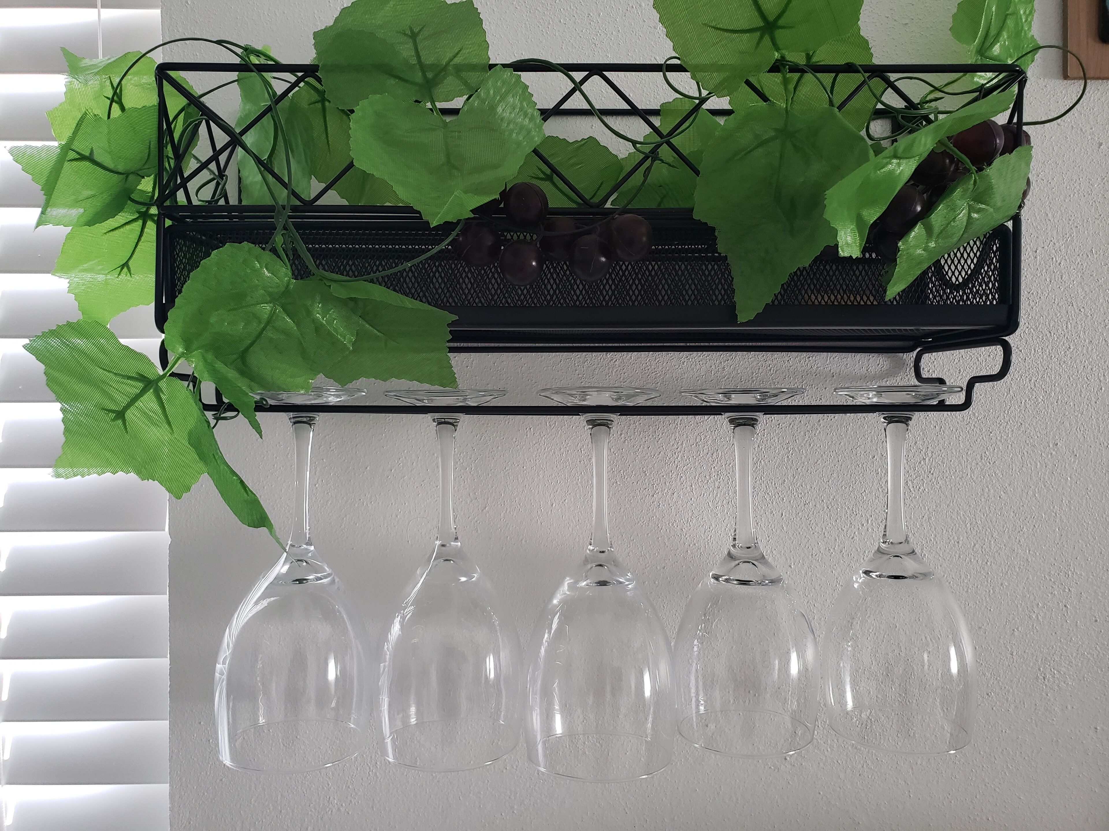 A black metal rack with green leaves and clear wine glasses hanging from it.