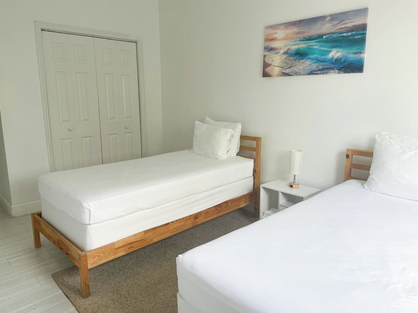 A bedroom with a single bed, a nightstand, a lamp, and a door.