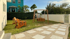 Un jardin avec une balançoire en bois, une pelouse et une maison à la façade bleue.
