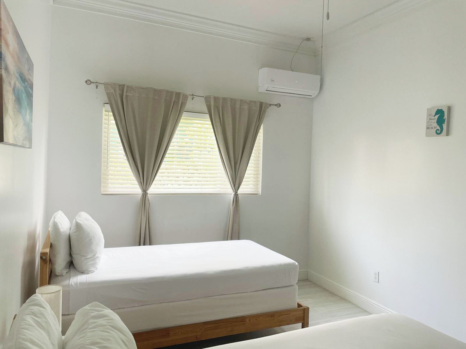 A bedroom with a bed, curtains, an air conditioning unit, and a wall-mounted artwork.