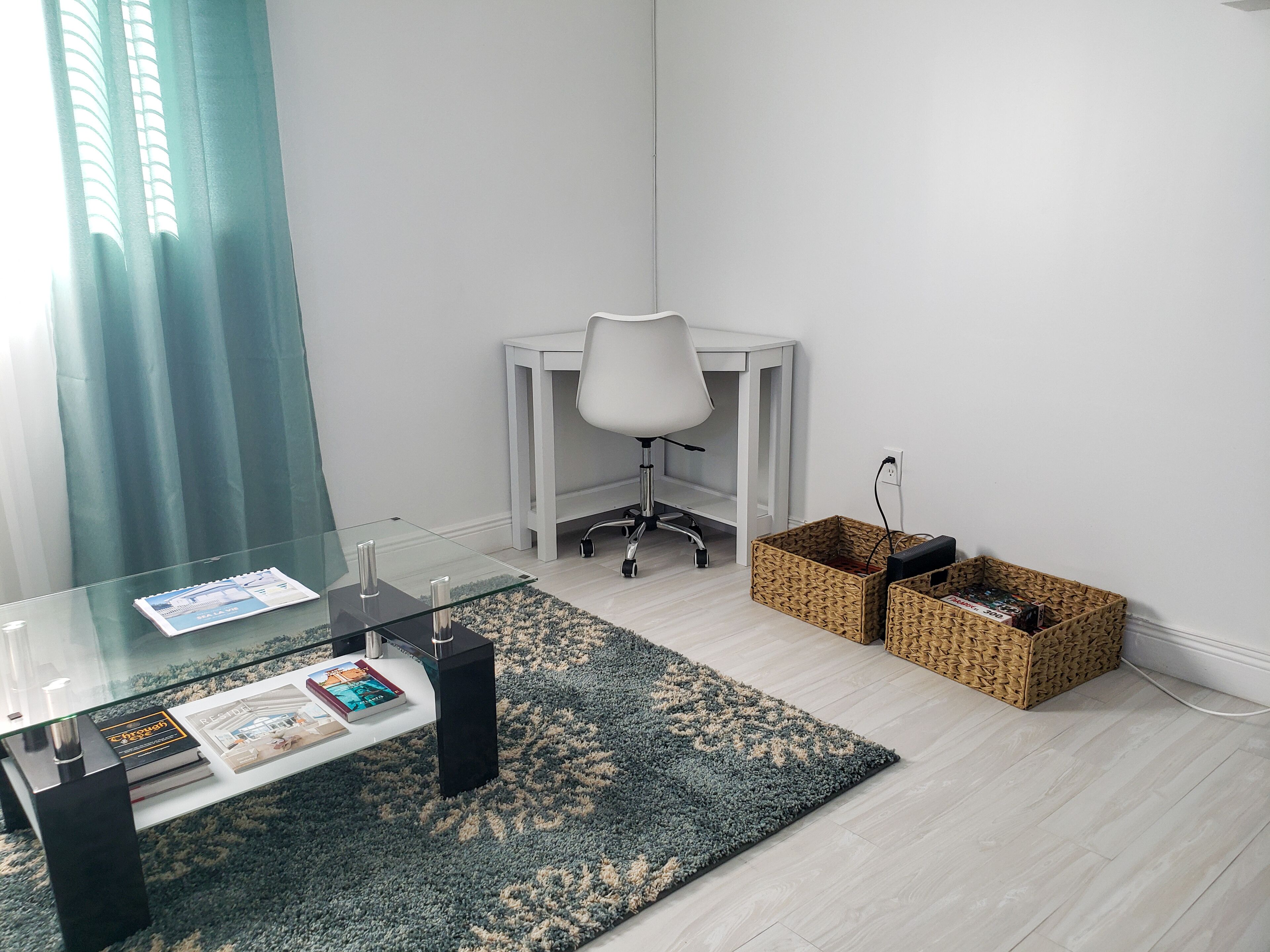 A modern room with a glass coffee table, a white office chair, a patterned rug, and wicker storage boxes.
