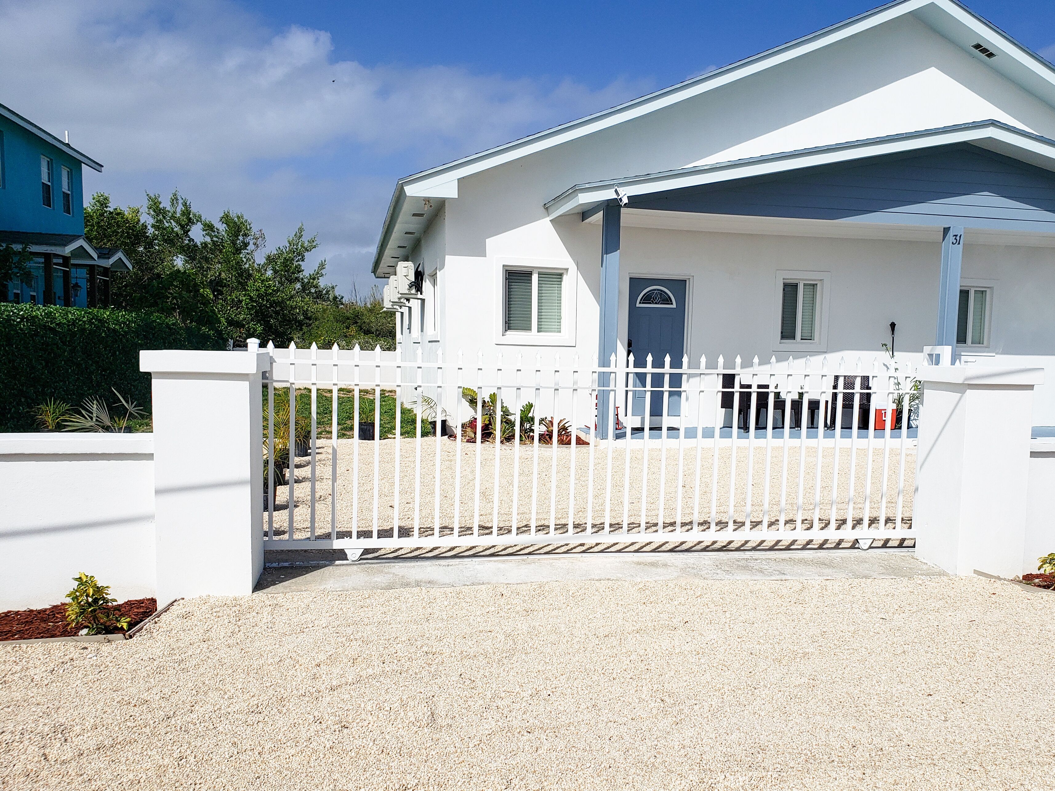 Une maison blanche avec une porte bleue, une clôture blanche et une allée gravillonnée.