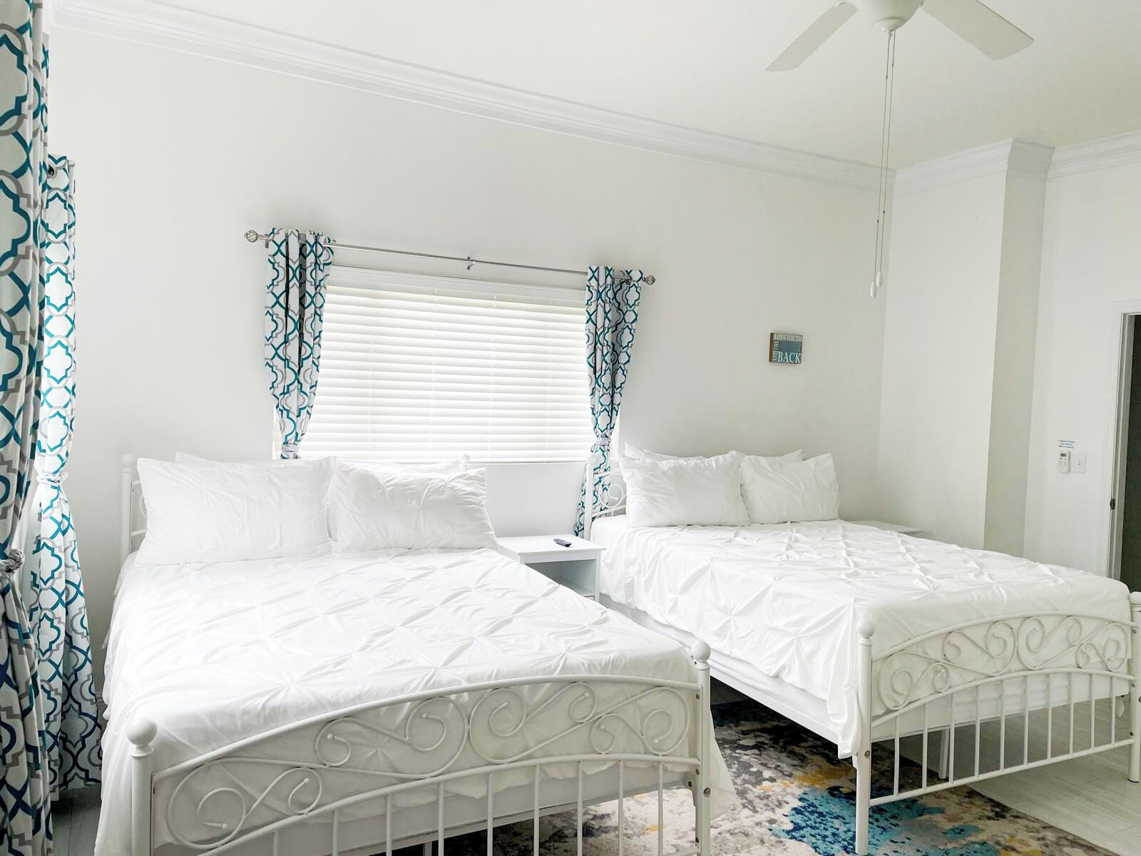 A bedroom with two beds, white bedding, a ceiling fan, and patterned curtains.