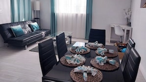 Un salon moderne avec un canapé en cuir noir, une table à manger en verre agrémentée de sets de table en fibres tressées, et un bureau blanc avec une chaise.