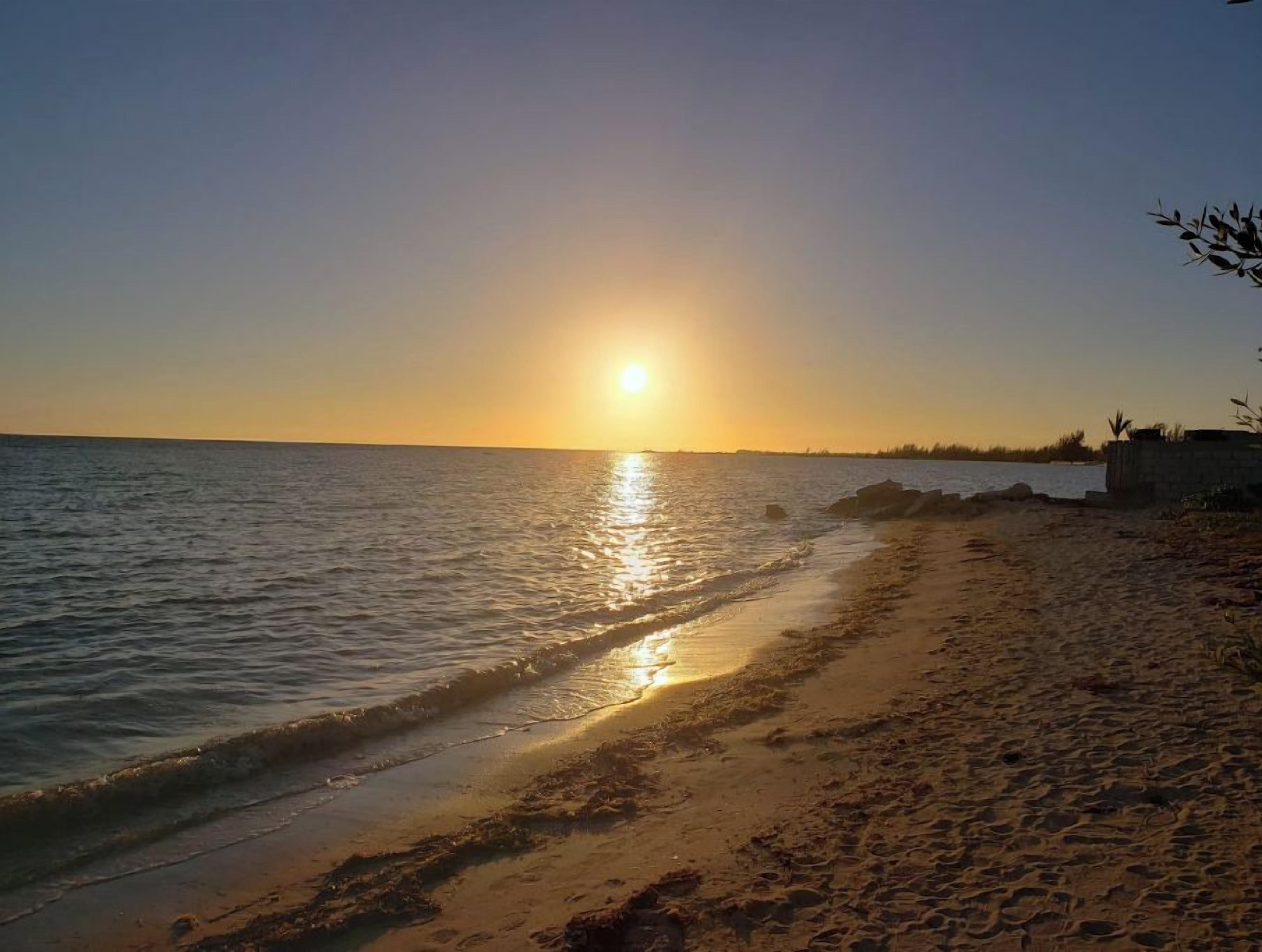 A beach at sunset with the sun reflecting on the water.