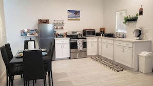 Une cuisine compacte avec des meubles blancs, un réfrigérateur, un four à micro-ondes et une cuisinière. On y trouve une table à manger avec des chaises et un petit tapis sur le sol.