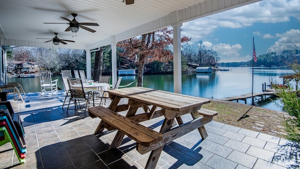 Eine überdachte Terrasse mit Holztisch und -stühlen, mit Blick auf einen See mit einer Anlegestelle und einer amerikanischen Flagge.