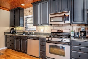 A kitchen with dark cabinets, a stainless steel microwave, a gas stove, and a dishwasher.