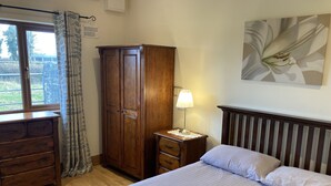 Une chambre à coucher comprenant un lit, une armoire en bois, une table de chevet avec une lampe, une commode et une fenêtre avec des rideaux.