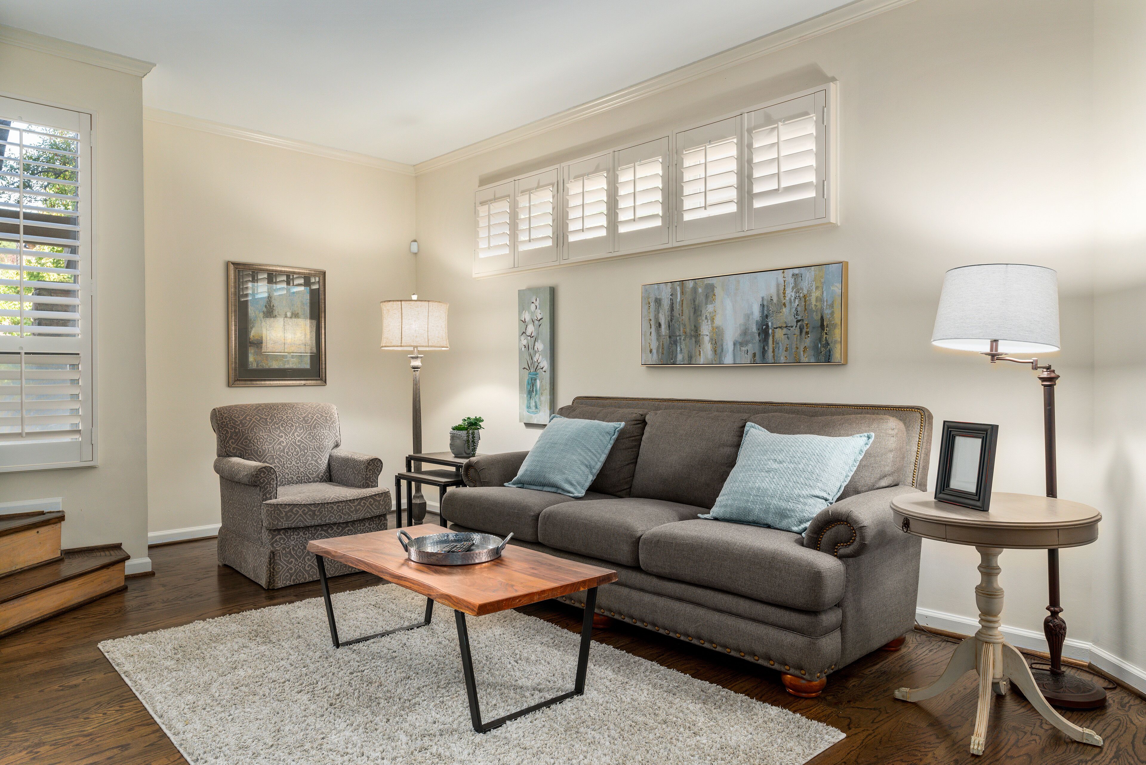 A living room with a gray sofa, a wooden coffee table, a lamp, and a painting on the wall.