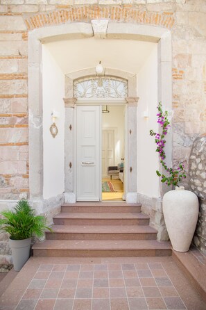 A stone building entrance with a white door, steps, and a potted plant. - Eressian Hotel & Hammam Spa (Lesvos)