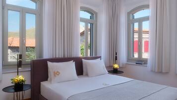 A hotel room with a large bed, two bedside tables, and a view of a red-roofed building through the windows.
